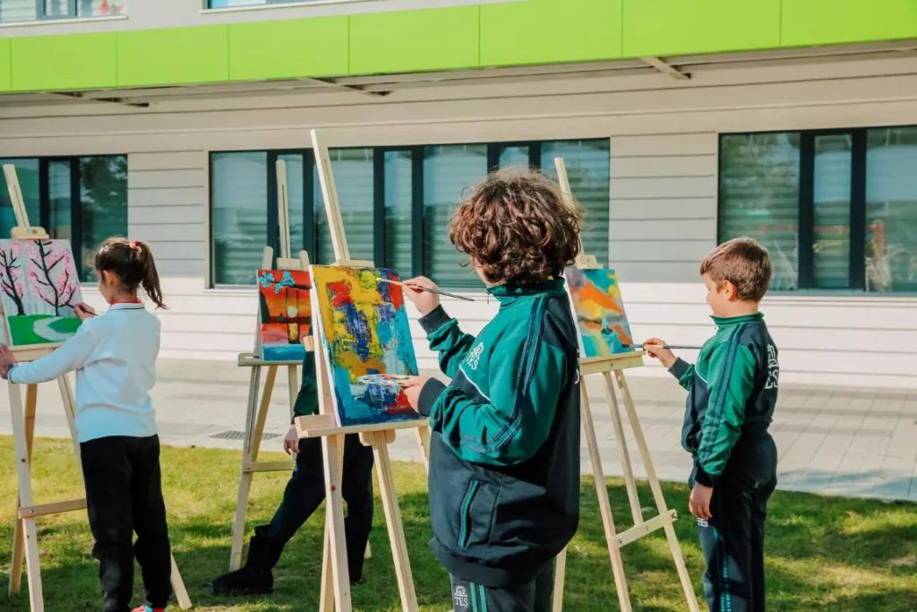 Un gruppo di ragazzi nel guardino della scuola che dipingono la natura su pannelli da disegno