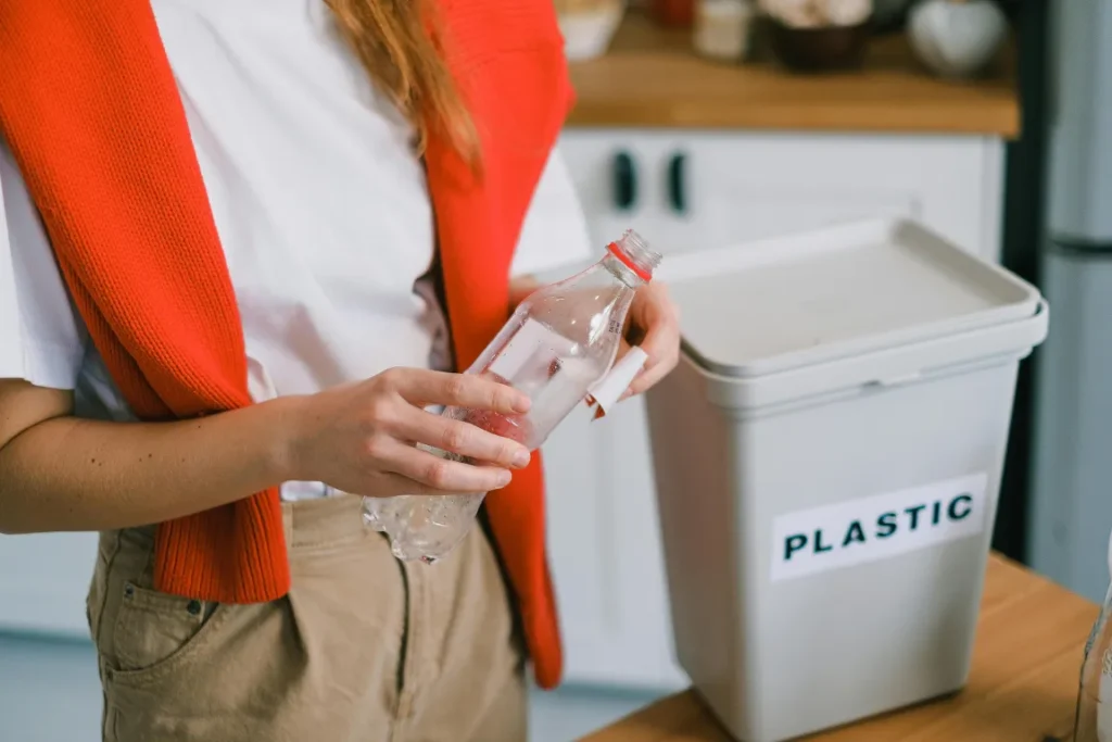 Una ragazza con in mano una bottiglia di plastica che sta buttando nel bidone della raccolta differenziata.