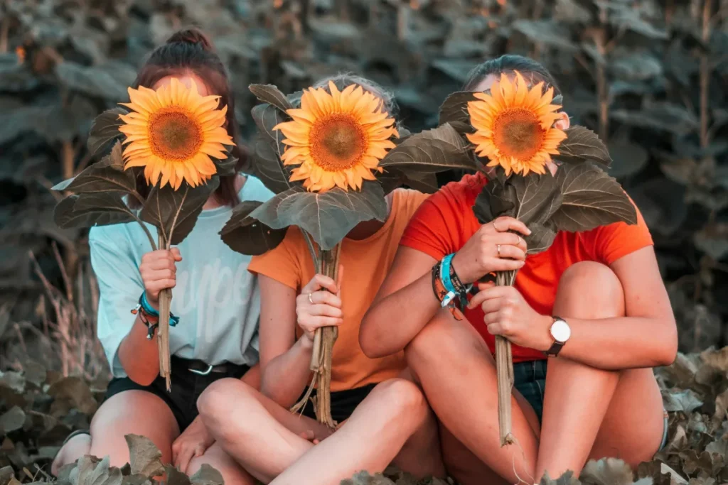 Foto di tre ragazze che tengono in mano un girasole con cui si coprono il viso.